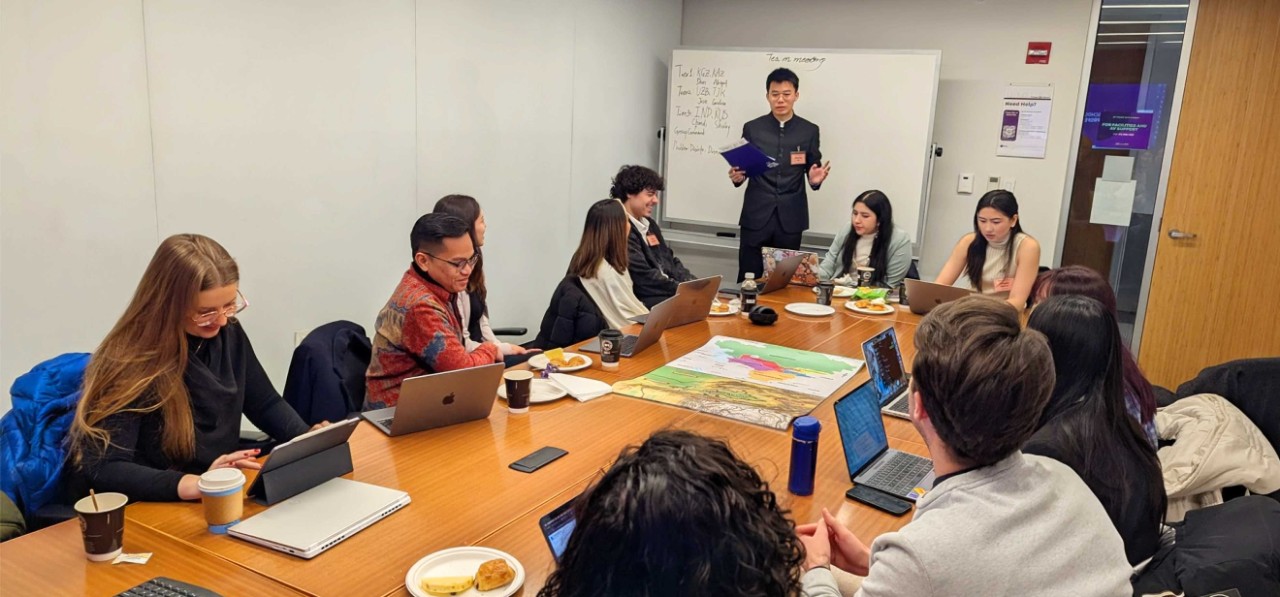 A group of people in a conference room having a meeting around a large table with laptops and notes.