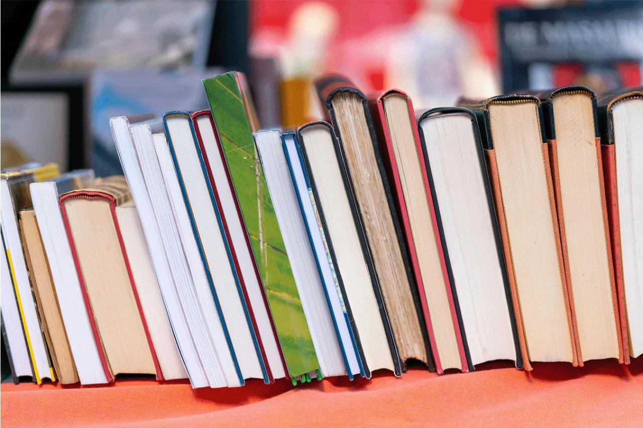 A row of used books with colorful covers and worn pages, leaning on a market stall covered with an orange cloth.