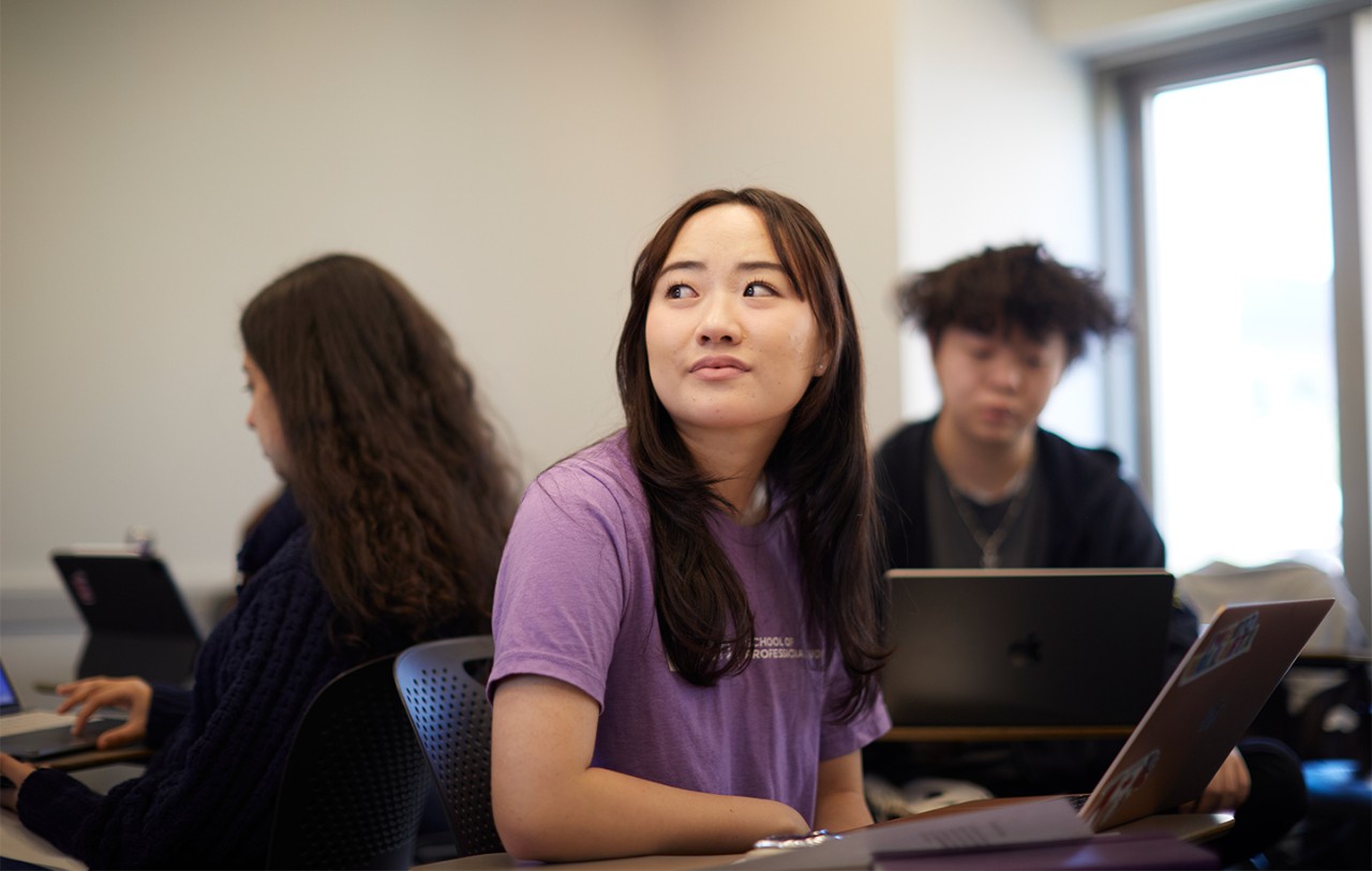 Students in a classroom, with a woman in a purple shirt looking to the side.