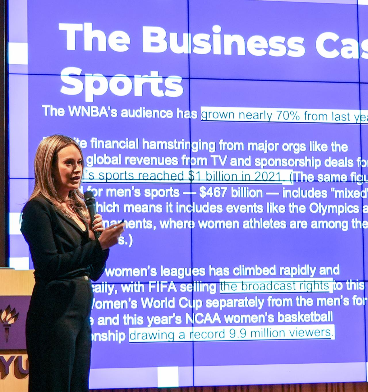 A woman presents a keynote speech titled "The Business Case for Women in Sports" on stage during an event at NYU SPS.