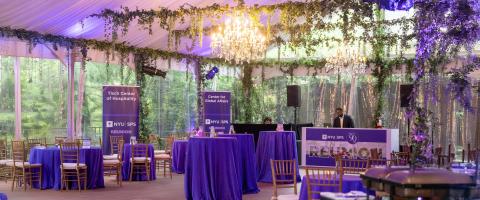 NYU SPS Reunion event space with purple tablecloths, chandeliers, and greenery decorations inside a tent.