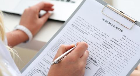 A woman fills out medical intake forms on a clipboard.