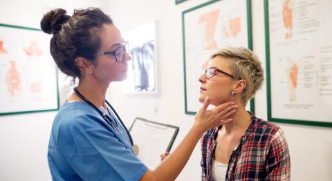 A healthcare provider examines a seated patient's neck in an exam room.