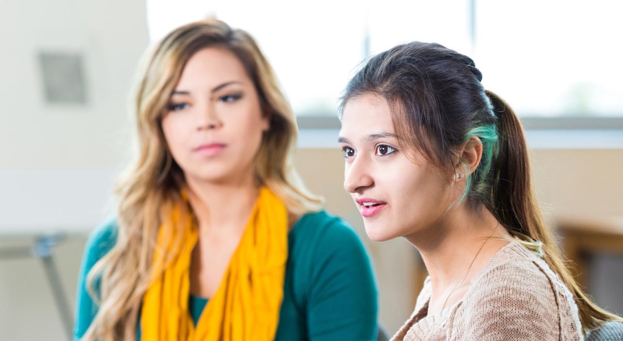 Two women sit in a medical waiting room, gazing to the left of the camera.
