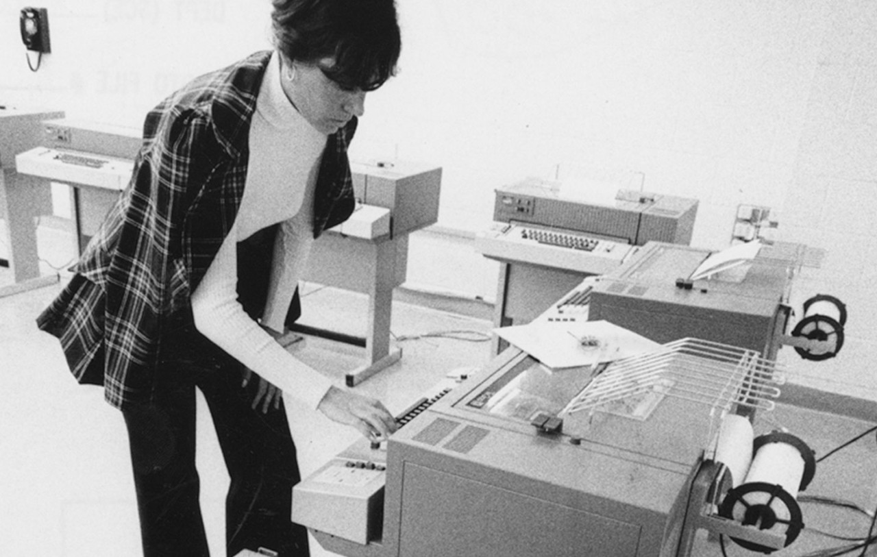 A woman working with vintage computing equipment in a retro data processing room.