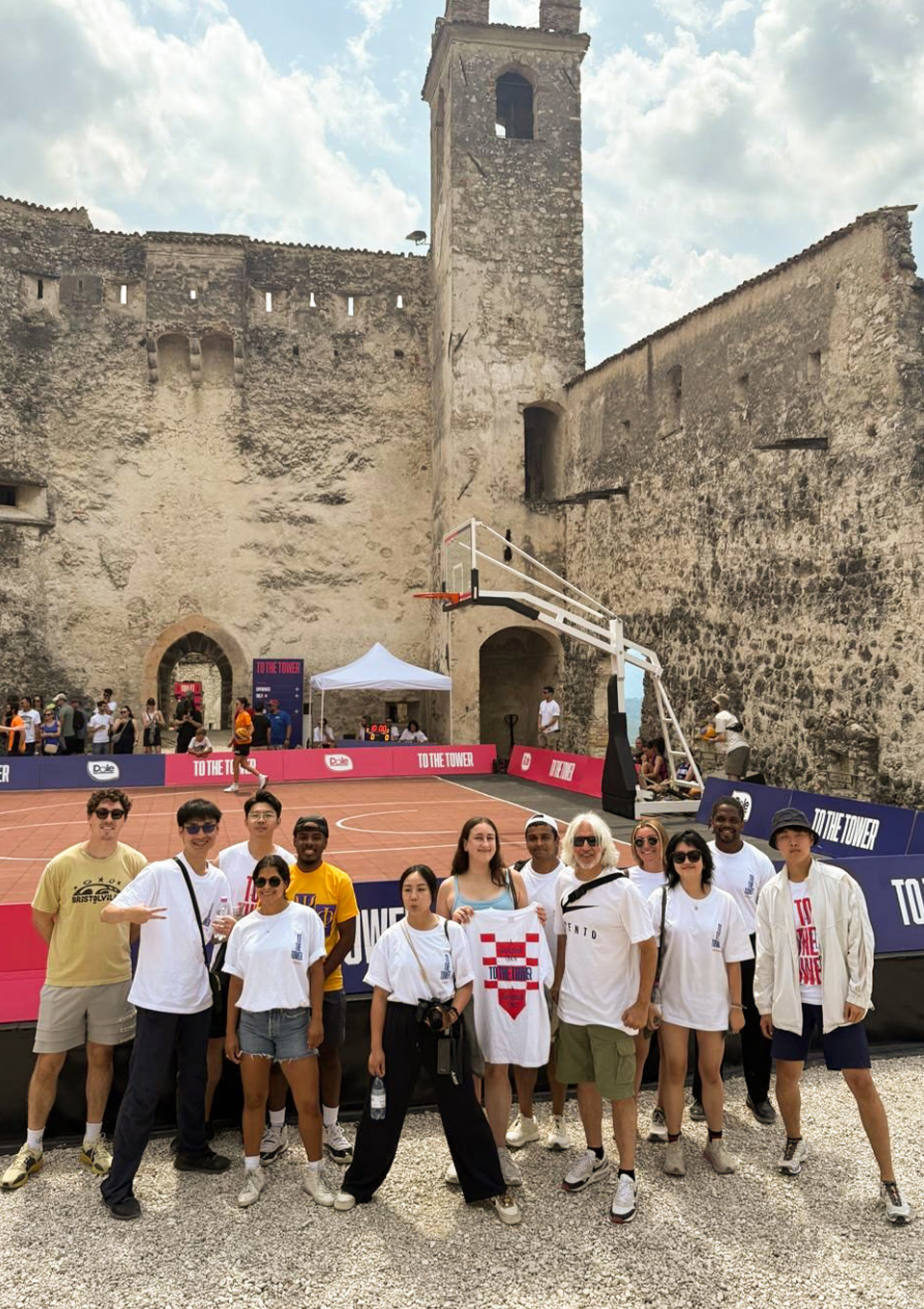 A group of people pose in front of an outdoor basketball court set against an ancient stone fortress.