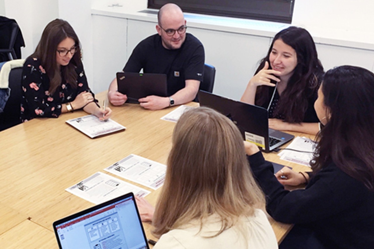 Students sit at a table reviewing laptops and papers.
