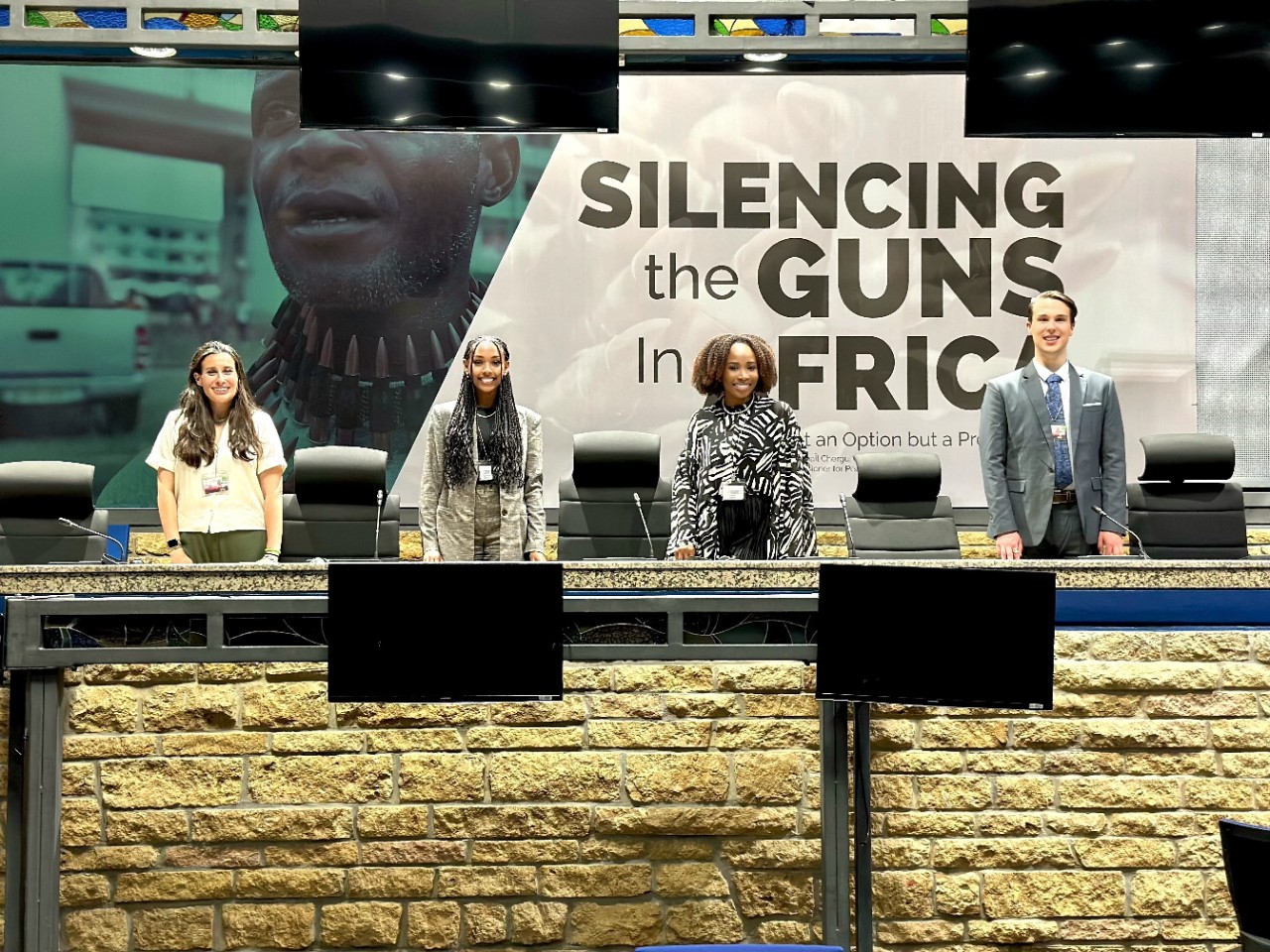 Four CGA attendees stand in front of a sign that reads, 'Silencing the Guns in Africa.'