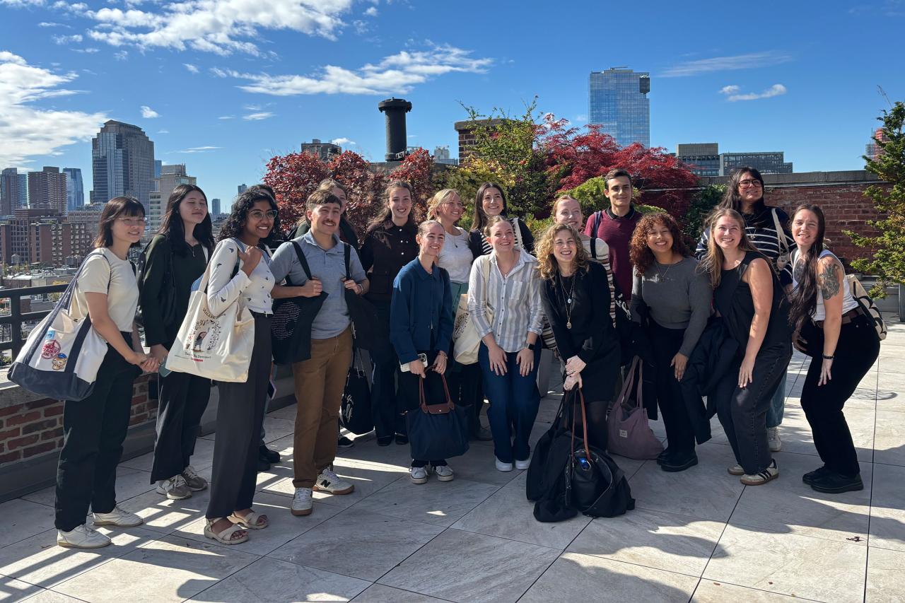 A group of fifteen people smiling on a sunny rooftop.