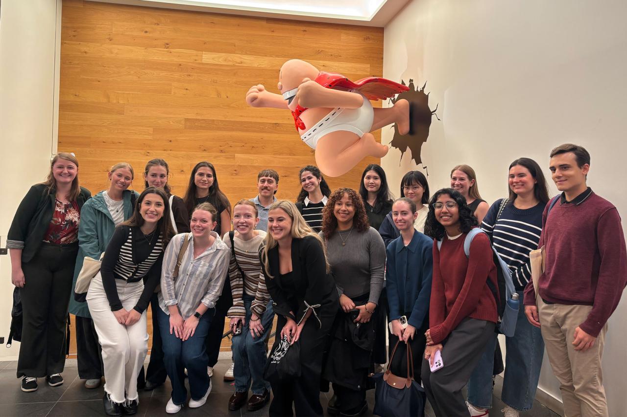 A group of smiling people poses in front of a large cartoon character, Captain Underpants, bursting through a wooden wall.