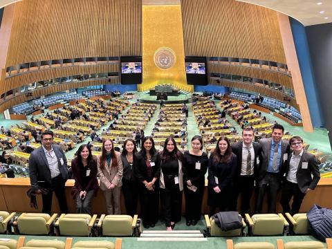 Students and faculty standing together inside the United Nations General Assembly Hall, overlooking the chamber and delegates seated below.