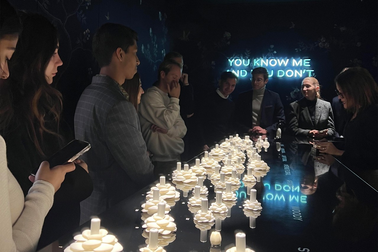 A group of people stand around an elegant, dimly lit table adorned with cream-colored decorative candles.