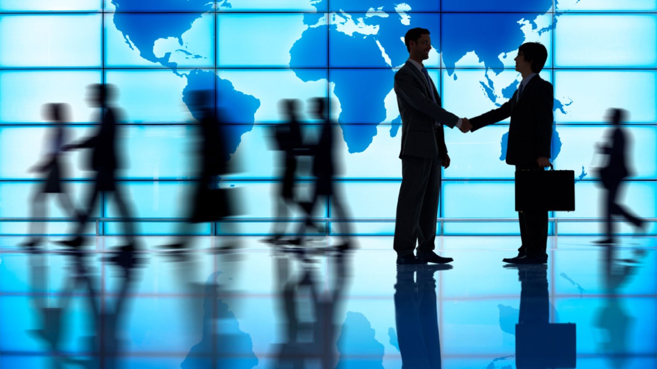 Business professionals shaking hands in front of a large world map display, symbolizing global collaboration and international partnerships.
