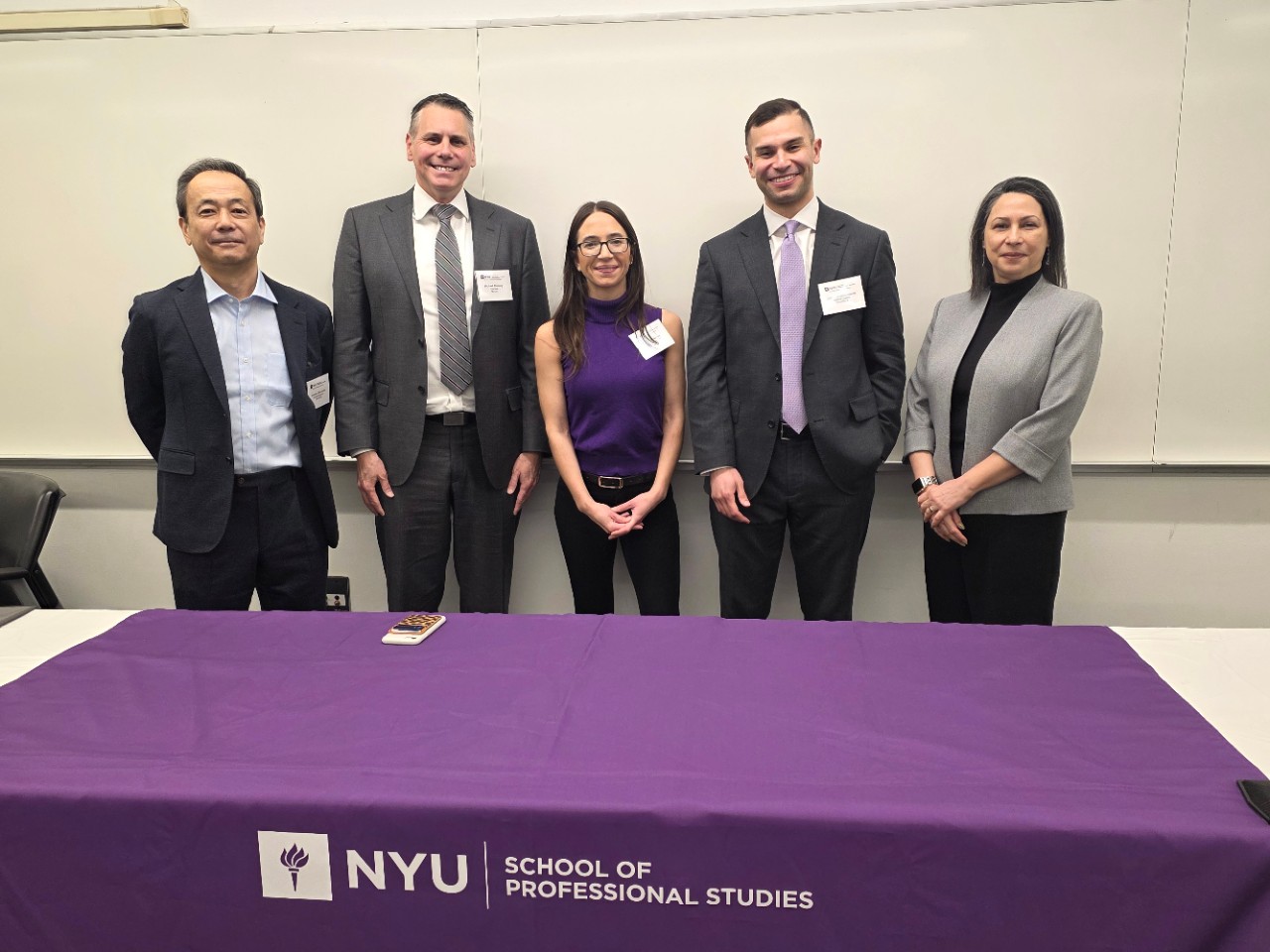 Panelists and Assistant Dean pose in front of NYU SPS tablecloth