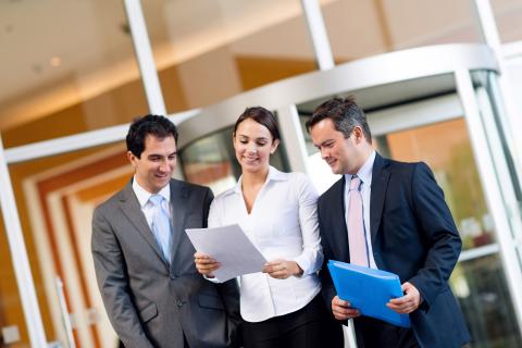 Three business professionals reviewing documents together outside a modern university building entrance