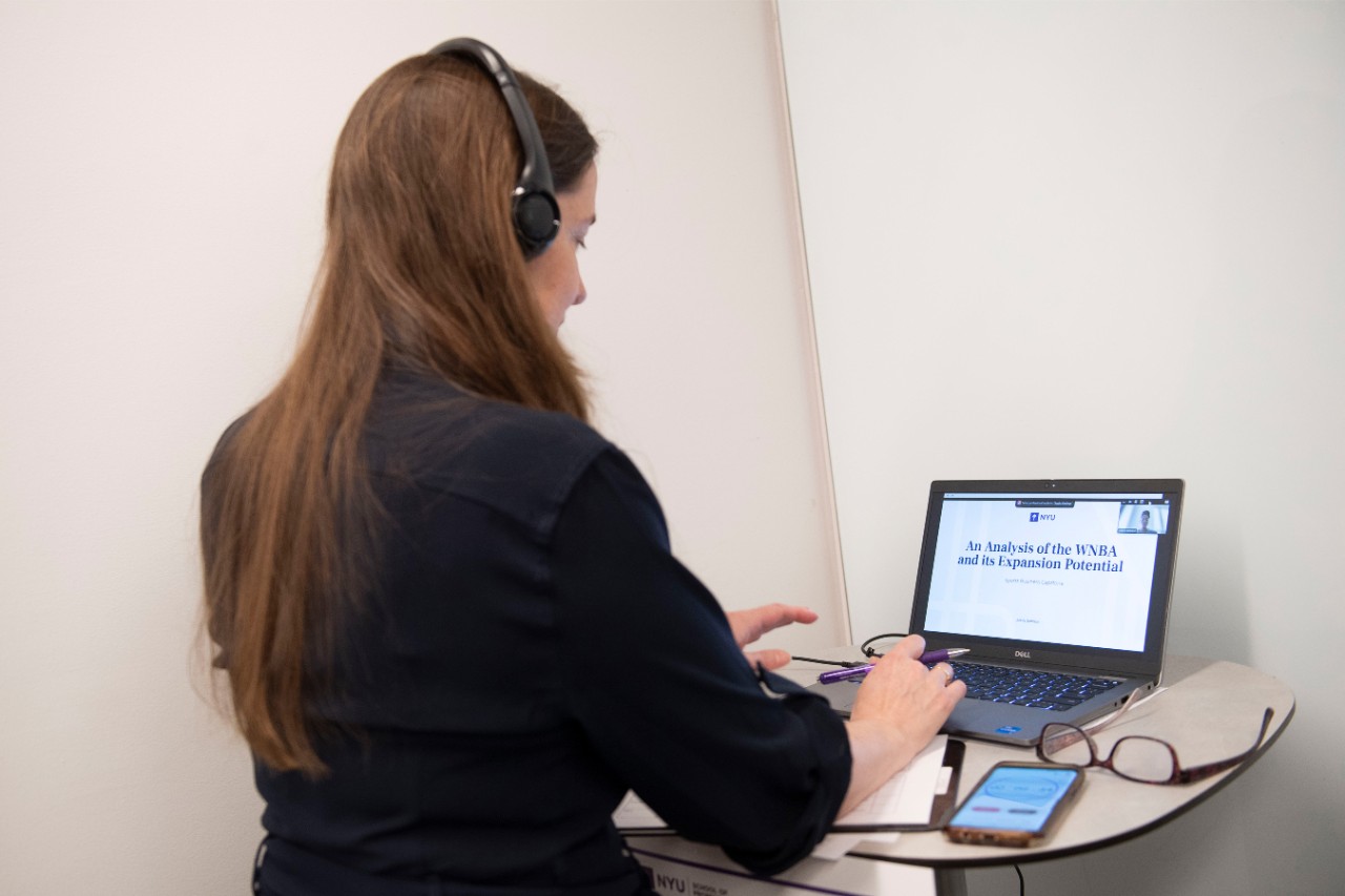 An NYU SPS student works on her capstone project titled "An Analysis of the WNBA and its Expansion Potential" on her laptop.
