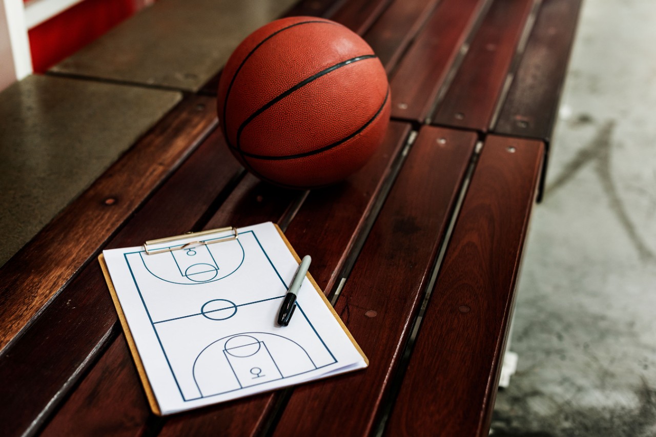 Basketball and diagram of a basketball court sitting on top of a court side bench.