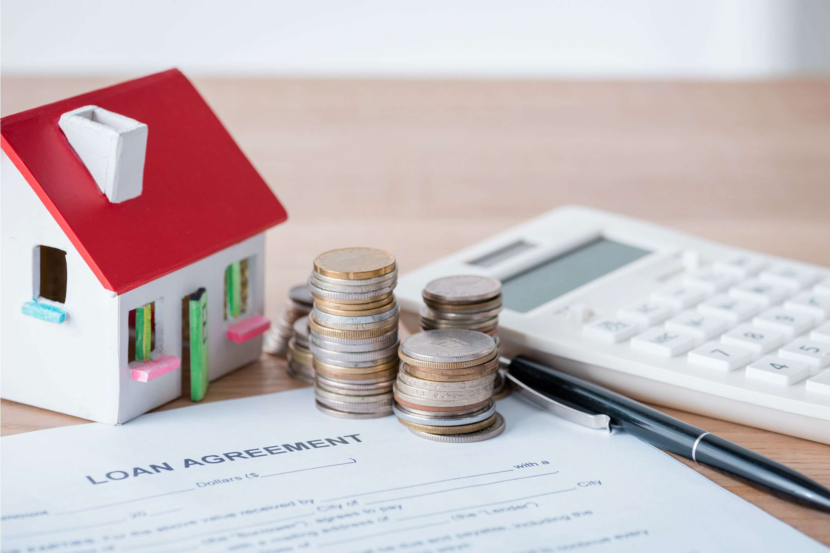 Model House, coins, loan agreement, black pen, and calculator on top of a wooden surface.