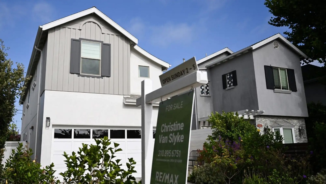 Modern two-story house with a "For Sale" sign in front, advertising an open house on Sunday. The home features gray and white siding with black shutters.