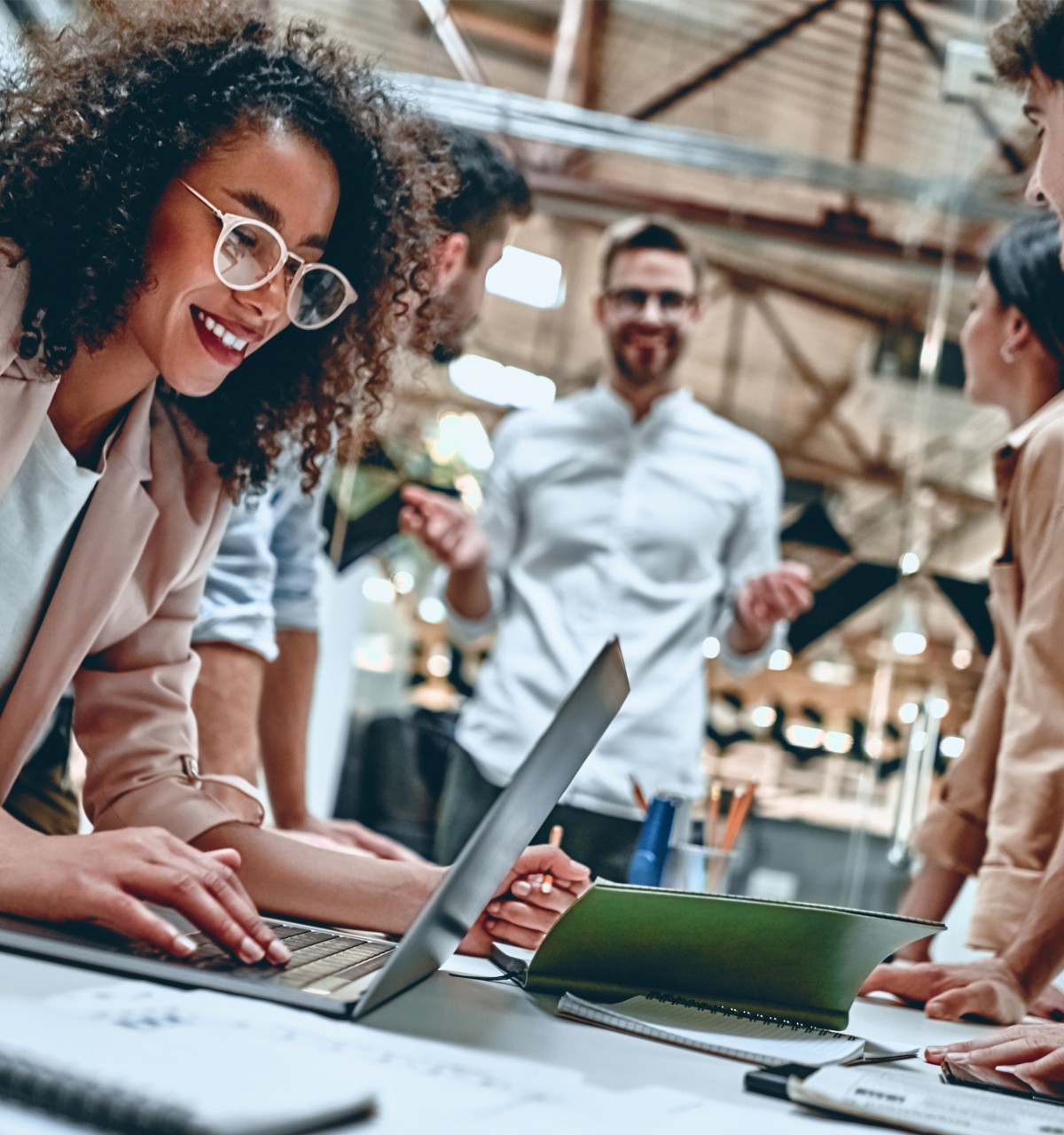    A classroom filled with students; one group chats at a table, another explores VR with headsets. A screen displays interactive content.