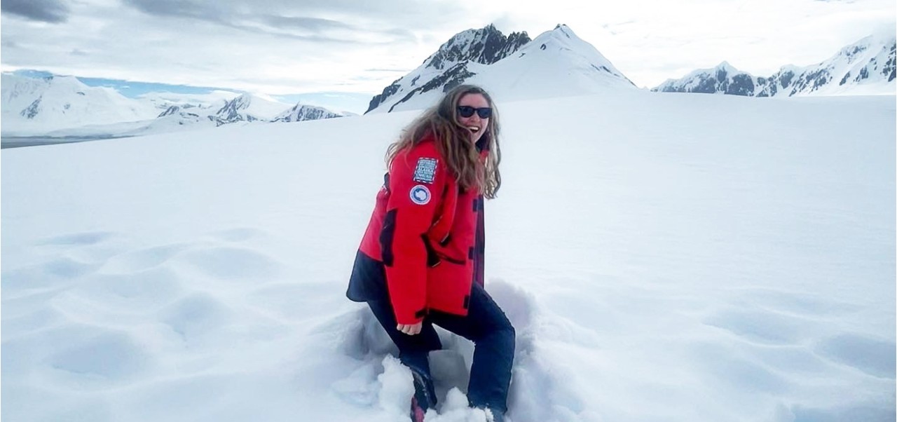 Alex Day, NYU SPS Preston Robert Tisch Institute for Global Sport alumnus, laughs while standing in knee-high snow amidst mountains.