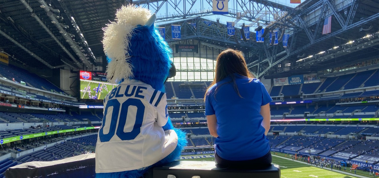 Alexa Strobridge, Tisch Center for Global Sport alumnus at NYU SPS, sits in an empty soccer arena with a team mascot.