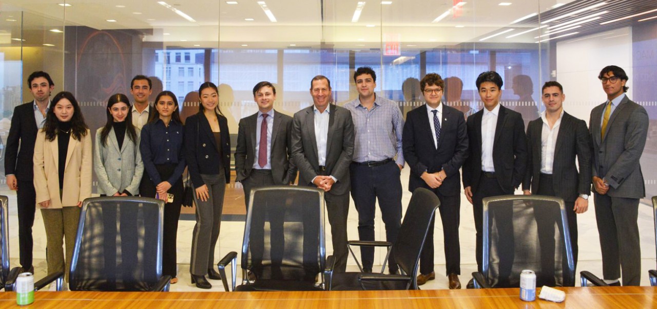 Harrison Koeppel, Schack Institute at NYU SPS alumnus, poses for a photo alongside a large group of fellow students in a modern office space.