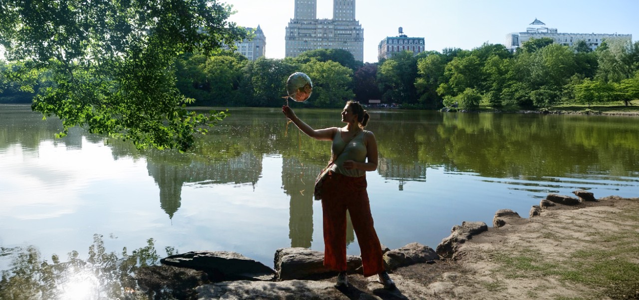 Melanie Stavenow, Center for Global Affairs at NYU SPS alumnus, artfully manipulates a large bubble near a pond in Central Park.