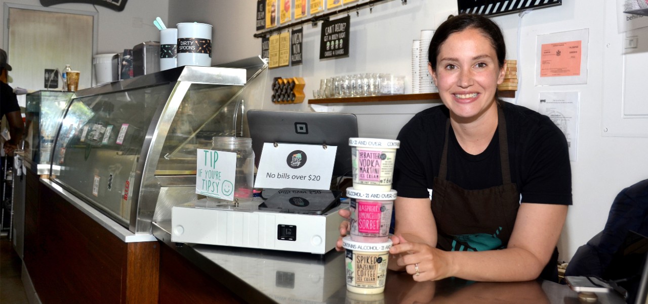 Melissa Tavss, Division of Programs in Business at NYU SPS alumnus, takes a break from working at her ice cream shoppe to smile for the camera with a selection of unique flavors.