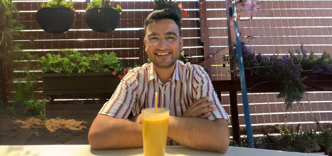Division of Programs in Business at NYU SPS alumnus Prithviraj Rathore smiles for the camera while enjoying a large juice on a cafe terrace.