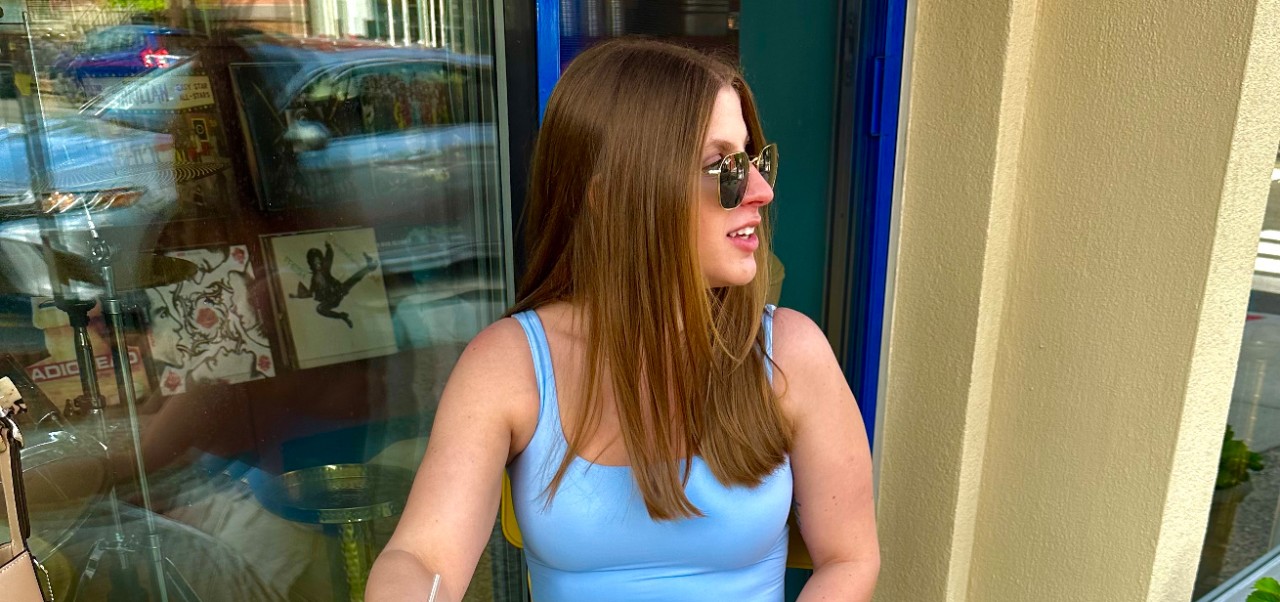 Rebecca Bodtmann, Preston Robert Tisch Institute for Global Sport alumni at NYU SPS, looks off to the right of the camera while wearing sunglasses and seated.