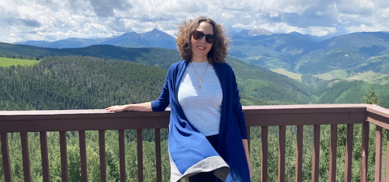 Rochelle Hestnas, Division of Applied Undergraduate Studies alumnus at NYU SPS, poses for the camera while standing on a deck overlooking forested mountains.