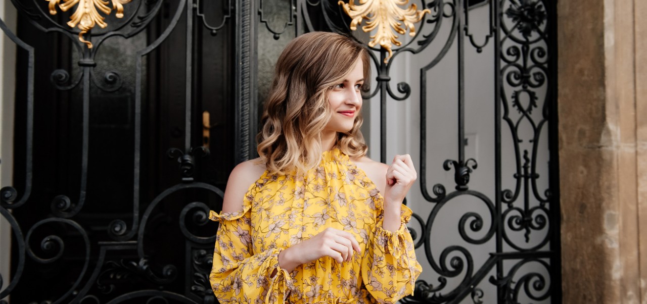 Roksolana Maria Sheverack, NYU SPS Division of Programs in Business alumnus, poses for a photo in front of a wrought-iron gate with ornamental gold accents.
