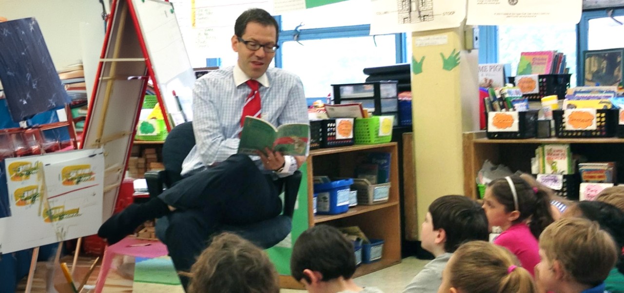 Adam Braff, Adjunct Instructor of Marketing and Public Relations at NYU SPS,  reads aloud from a book to a classroom full of children.