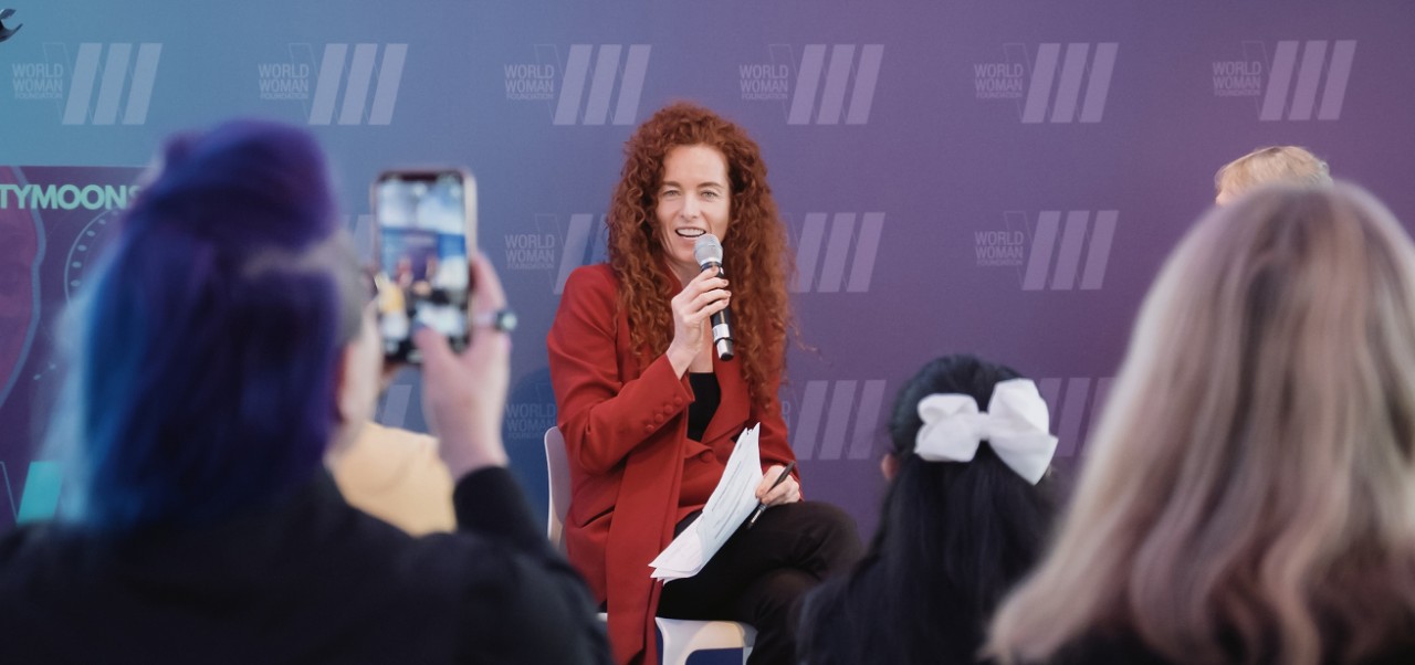 Carolyn Kissane, Clinical Professor, Center for Global Affairs at NYU SPS, gives a presentation while seated on-stage at a conference.