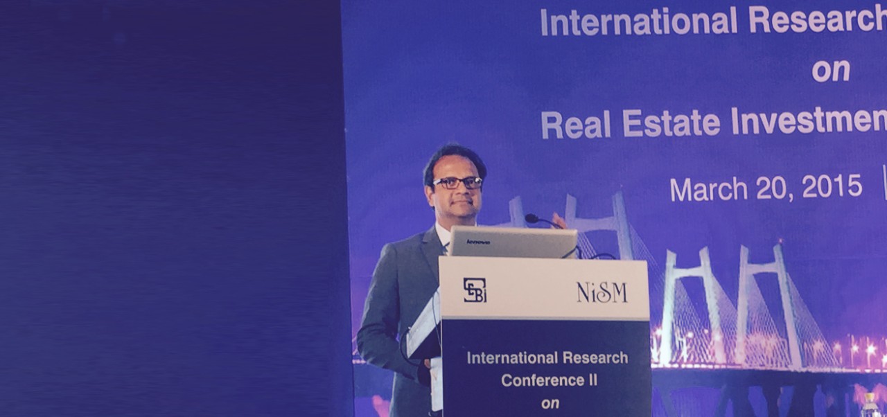 Manish Srivastava, Clinical Professor of Global Real Estate Finance, Investments, and Urban Development at the Schack Institute of Real Estate, NYU SPS, gives a presentation at a lectern during a 2025 conference on real estate.