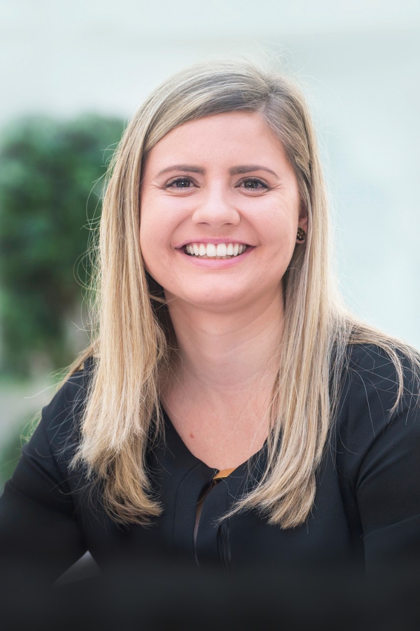 McKenna Schray smiles for a headshot while wearing a black long sleeve shirt with a white and green background