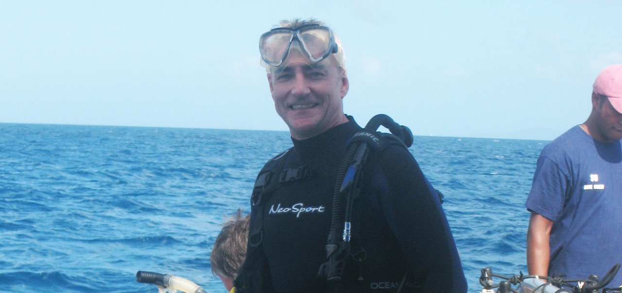 On a boat in the ocean, Paul Meadows smiles while wearing a scuba diving outfit