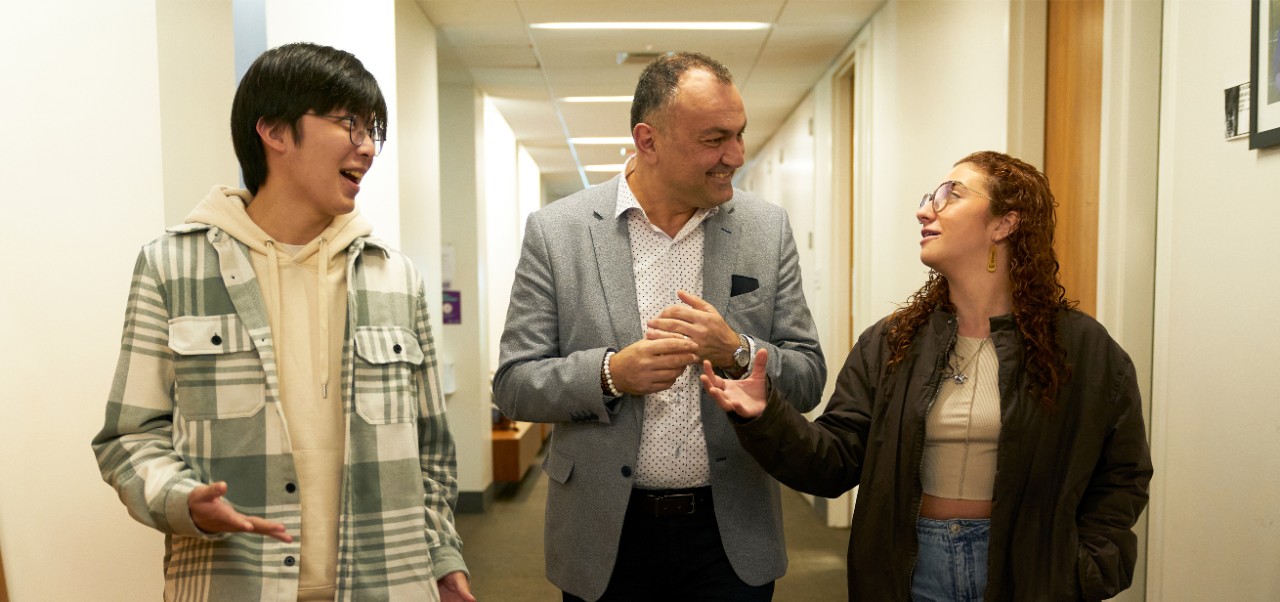Recep Karaburun walks through a hallway while having a conversation with a female student he is facing to his left and a male student to his right.