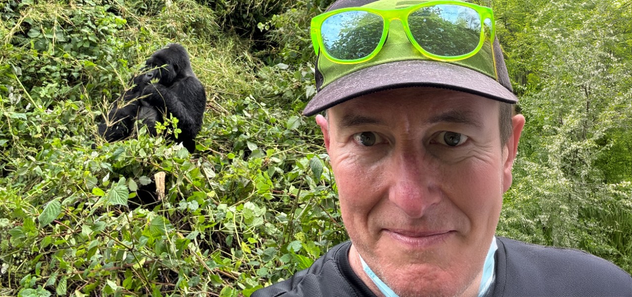 On a snowy mountaintop in Colorado, Scott Robinson wears green sunglasses and a helmet while taking a selfie with his red mountain bike behind him