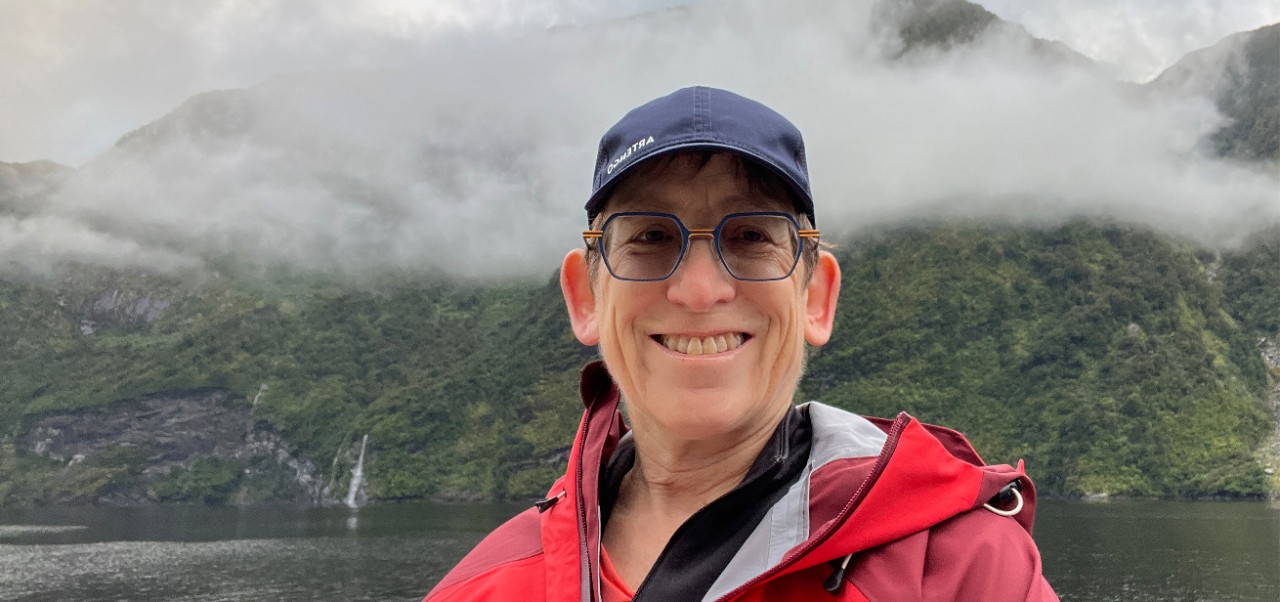 Susan Davies, Adjunct Assistant Professor, Center for Publishing and Applied Liberal Arts, NYU SPS, smiles for the camera while on vacation in a lush, forested, foggy landscape.