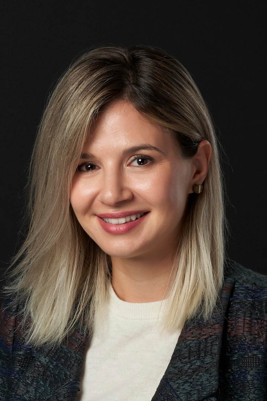 Wearing a blazer over a white shirt, Vanja Bogicevic smiles for a headshot in front of a black background