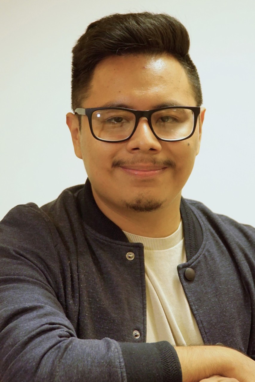 Jonathan Hernandez Jimenez smiles for a headshot wearing a dark grey jacket and tan shirt