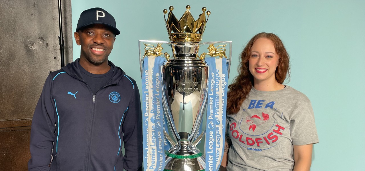 Morgan Baker, student at the NYU SPS Preston Robert Tisch Institute for Global Sport, poses for a photo alongside a large trophy for the Premiere League.