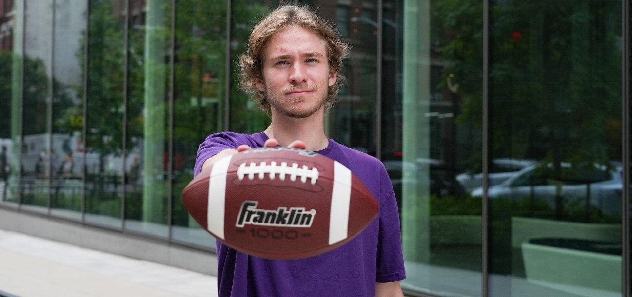 Peter Dicce, student at the Preston Robert Tisch Institute for Global Sport at NYU SPS, holds a football toward the camera while posing for a photo.