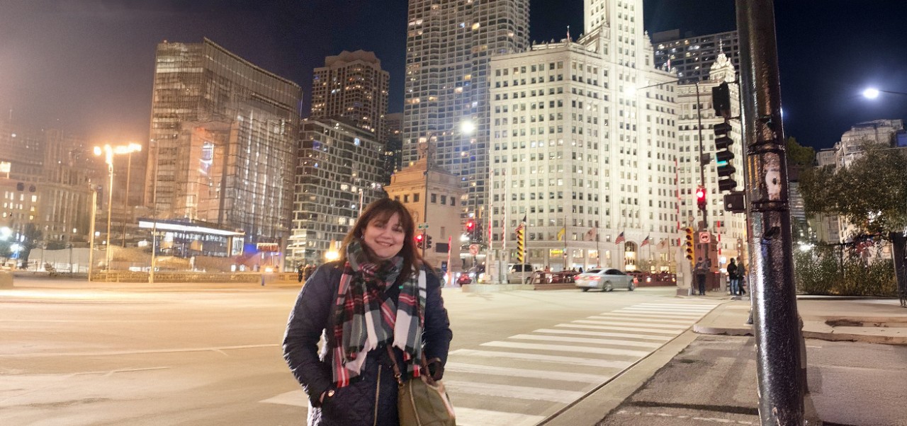 Reem Okar, student at the Center for Publishing and Applied Liberal Arts, NYU SPS, smiles for the camera in the middle of a busy urban intersection.