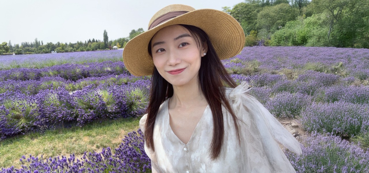 Victoria Guo, student at the NYU SPS Division of Programs in Business, poses for a photo in a field of lilac.