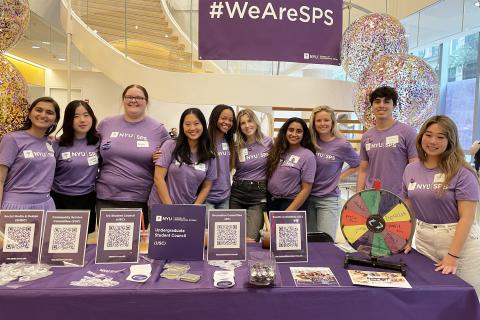 Students stand at a booth with pamphlets and other marketing materials.