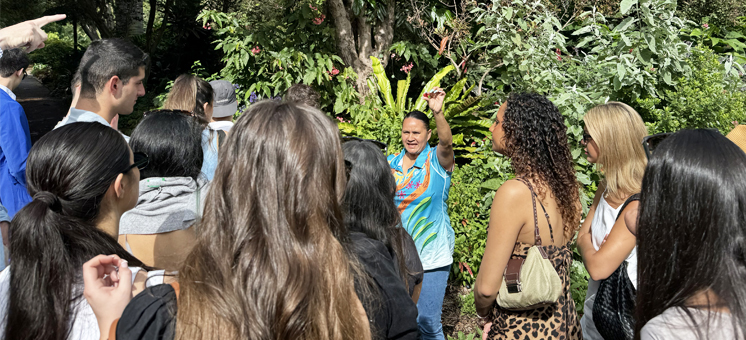 In Australia for a Global Field Intensive, a large group of BS in Real Estate students listen to a speaker outside in a jungle setting.