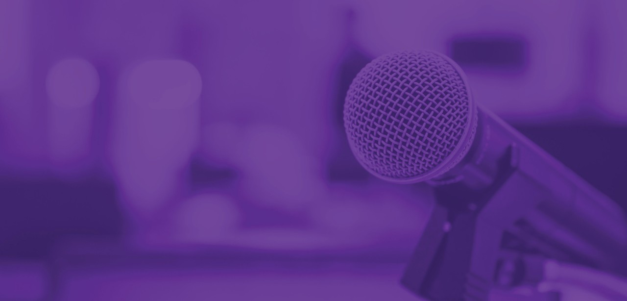 A woman draws on a transparent white board while demonstrating a business concept to colleagues seated at a table in the background.